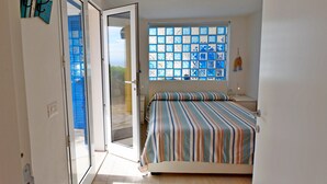 Een slaapkamer met een bed, een raam met uitzicht, een deur en een wand met een lamp.