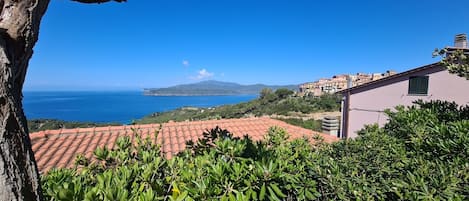 A coastal view with terracotta rooftops, a building with a green shutter, and a distant mountain.