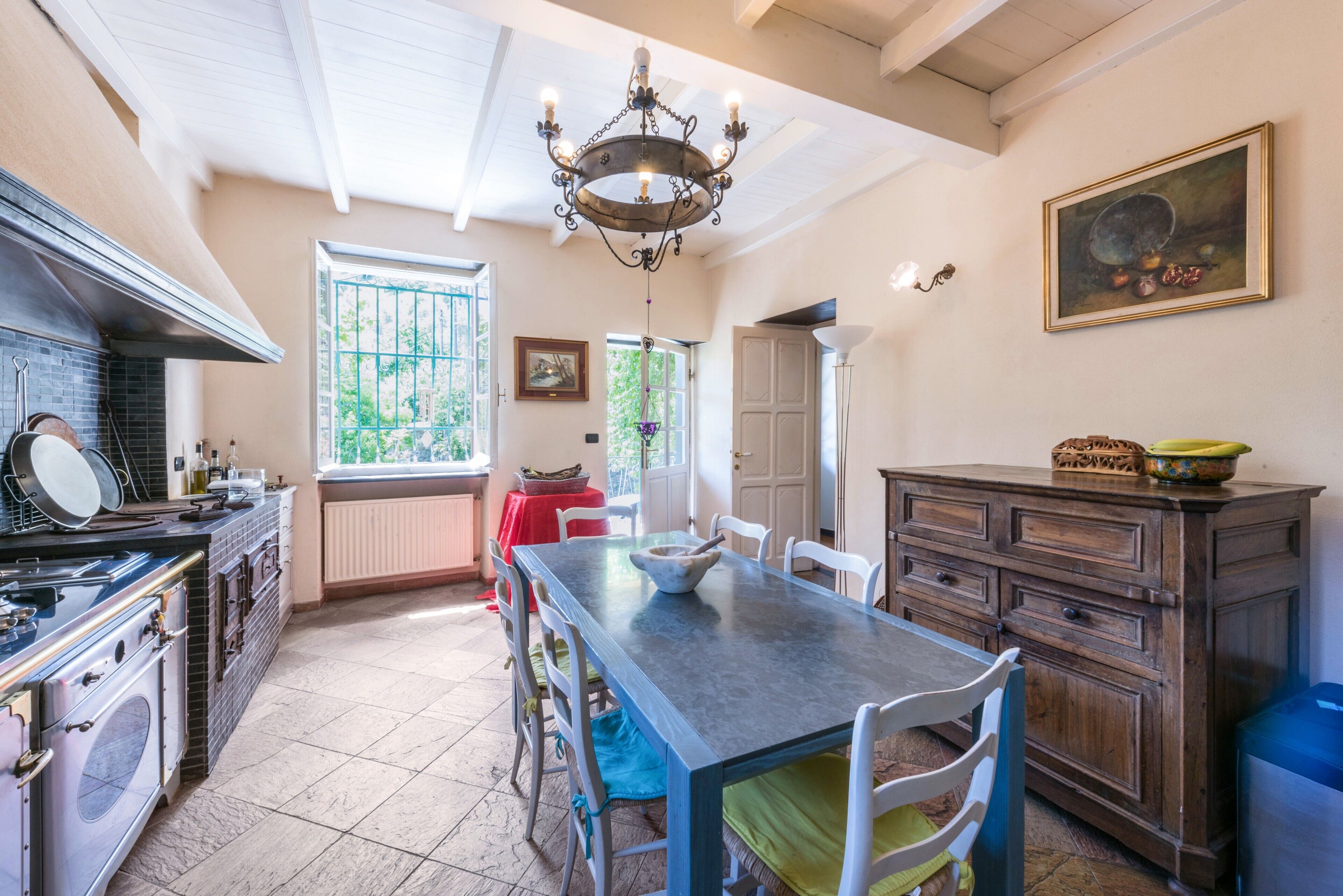 Una cocina con una mesa de comedor, sillas, una lámpara de araña y vistas al exterior.