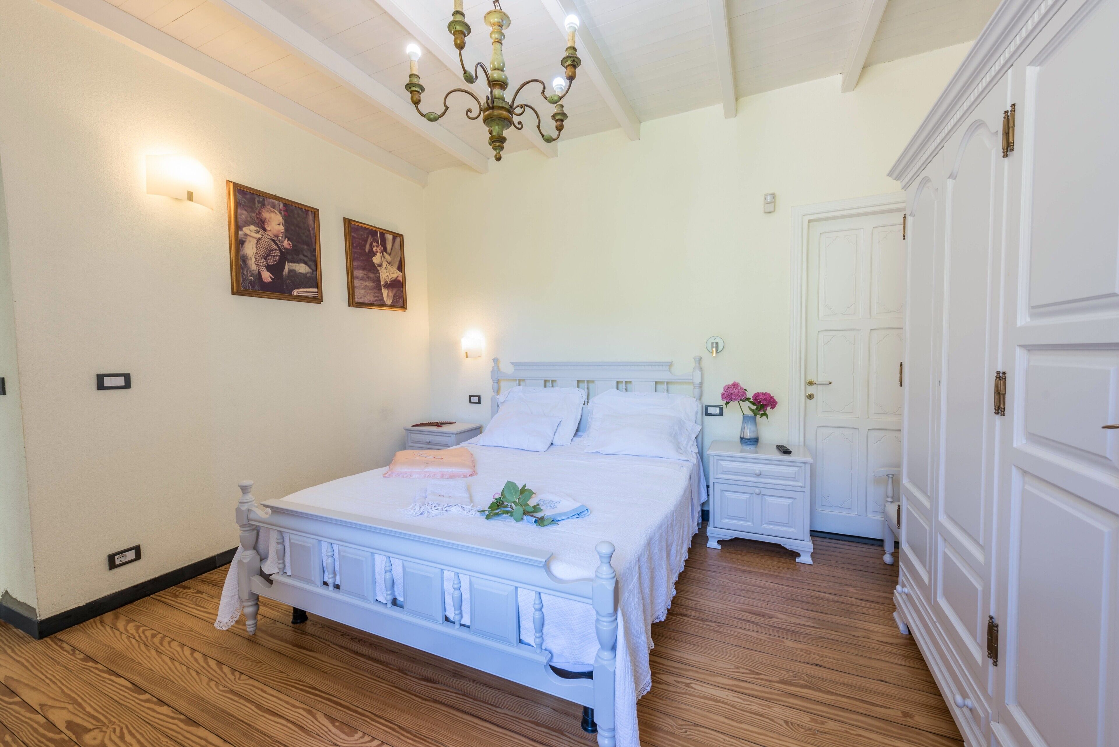 Ein Schlafzimmer mit einem weißen Bett, Holzboden, einer Chandelier und einem weißen Kleiderschrank.