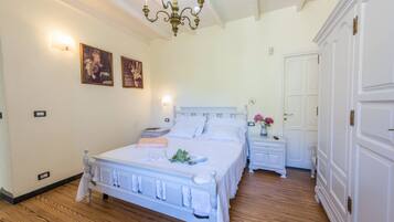 Ein Schlafzimmer mit einem weißen Bett, Holzboden, einer Chandelier und einem weißen Kleiderschrank.