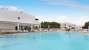 A swimming pool with lounge chairs and a covered area, surrounded by white buildings.