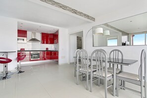Una cocina moderna con armarios rojos, un comedor con mesa de vidrio y sillas de metal, y un espejo grande que refleja la habitación.