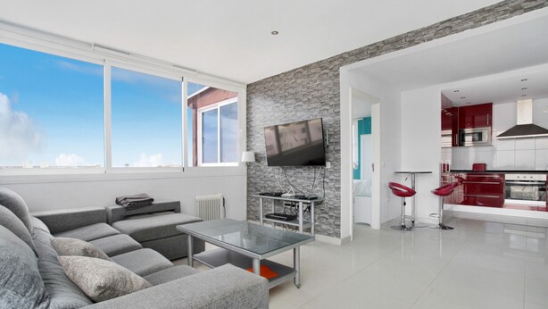 A modern living room with a grey sofa, a glass coffee table, and a TV mounted on a stone wall.