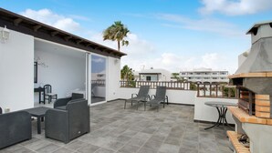 A rooftop patio with outdoor furniture, a grill, and a view of buildings in the distance.