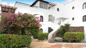 A white building with multiple balconies, a stone wall, and a tiled courtyard.