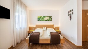 Un dormitorio con cama de madera, cortinas blancas, televisor montado, un cuadro enmarcado en la pared y un armario de madera.