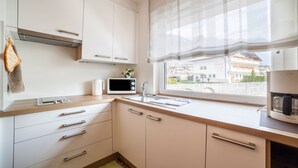 Una cocina con armarios blancos, microondas, cafetera y ventana con vista a edificios.