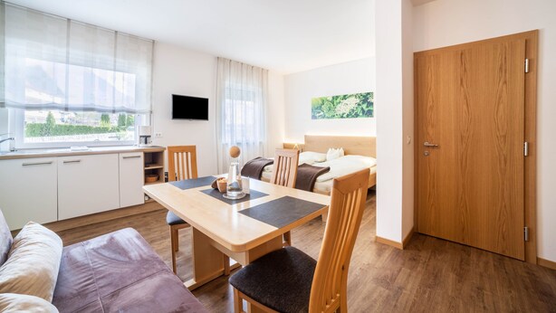 Una habitación moderna con una mesa de comedor de madera, un sofá, una cama, un televisor y una ventana con cortinas.