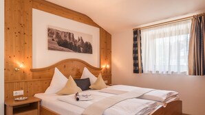 A wooden-framed bed with white bedding, a nightstand with a plate, and a wall-mounted picture. - Apartment 'Kristiania Type A2' with Mountain View, Sauna, Balcony & Garden (Siusi allo Sciliar (BZ))