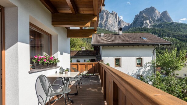 Ein Balkon mit Holzgeländer, einem Tisch mit Stühlen und einem Fenster mit Blumen.