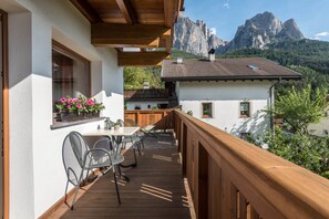 A balcony with a wooden railing, a table with chairs, and a window with flowers. - Kristiania Apartment Type A1 with Mountain View, Wi-Fi (Siusi allo Sciliar (BZ))