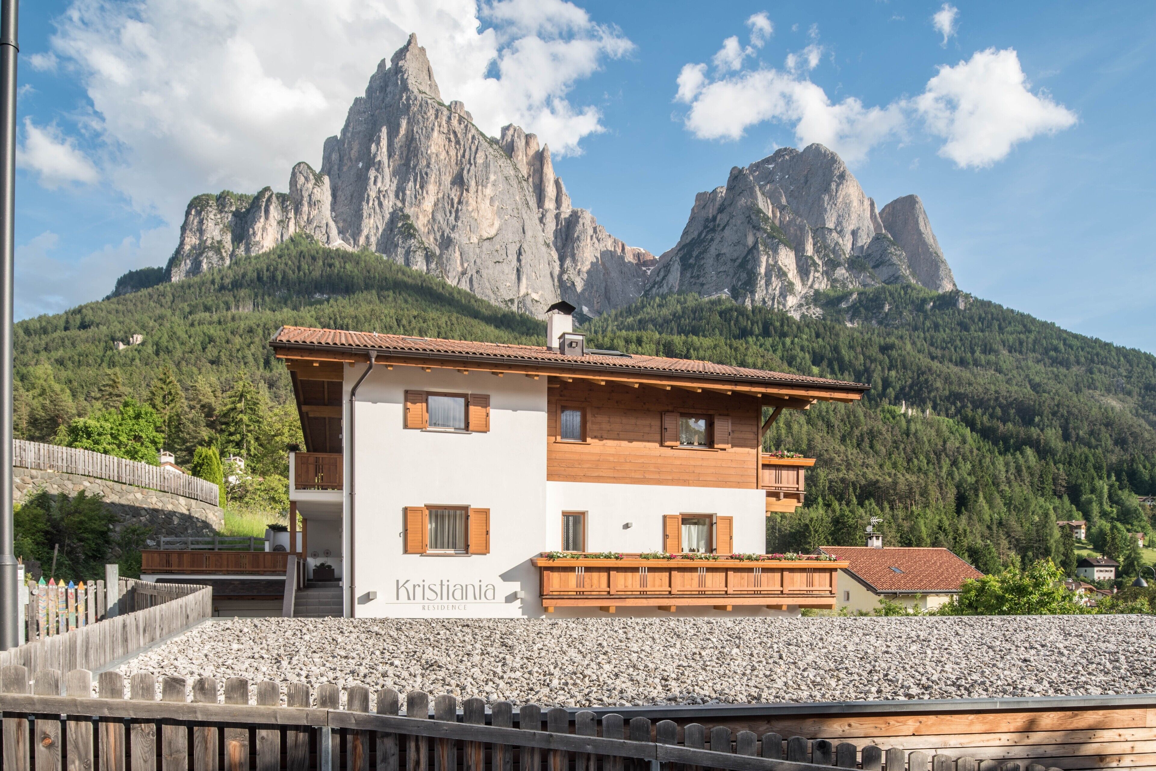 Ein zweistöckiges Gebäude mit einem Balkon, beschriftet mit 'Kristiania Residence', vor einer Bergkulisse.