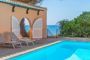 A swimming pool with lounge chairs, a pergola with white shutters, and a view of the sea. - Villa Lumb with Private Access to the Sea, Sea & Mountain View, Pool, A/C, Wi-Fi, Garden & Terrace (capdepera)