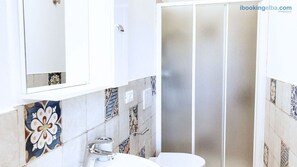 A bathroom with a white sink, a mirror, and a shower with frosted glass doors. - Appartamenti La Risacca - Appartamenti La Risacca Dependance n. 2 (Capoliveri)