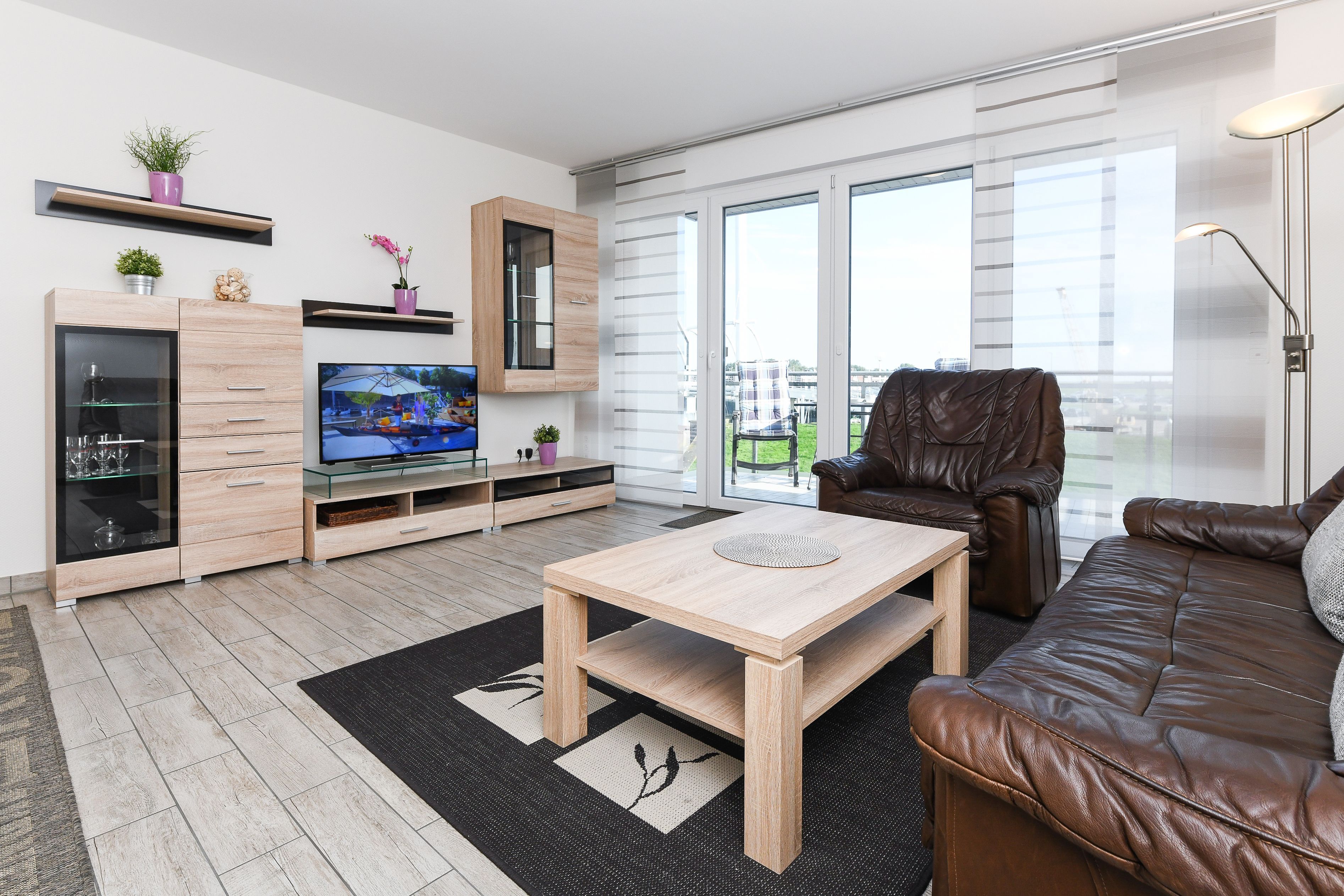 A modern living room with a wooden coffee table, leather sofa, and a TV on a wooden cabinet.