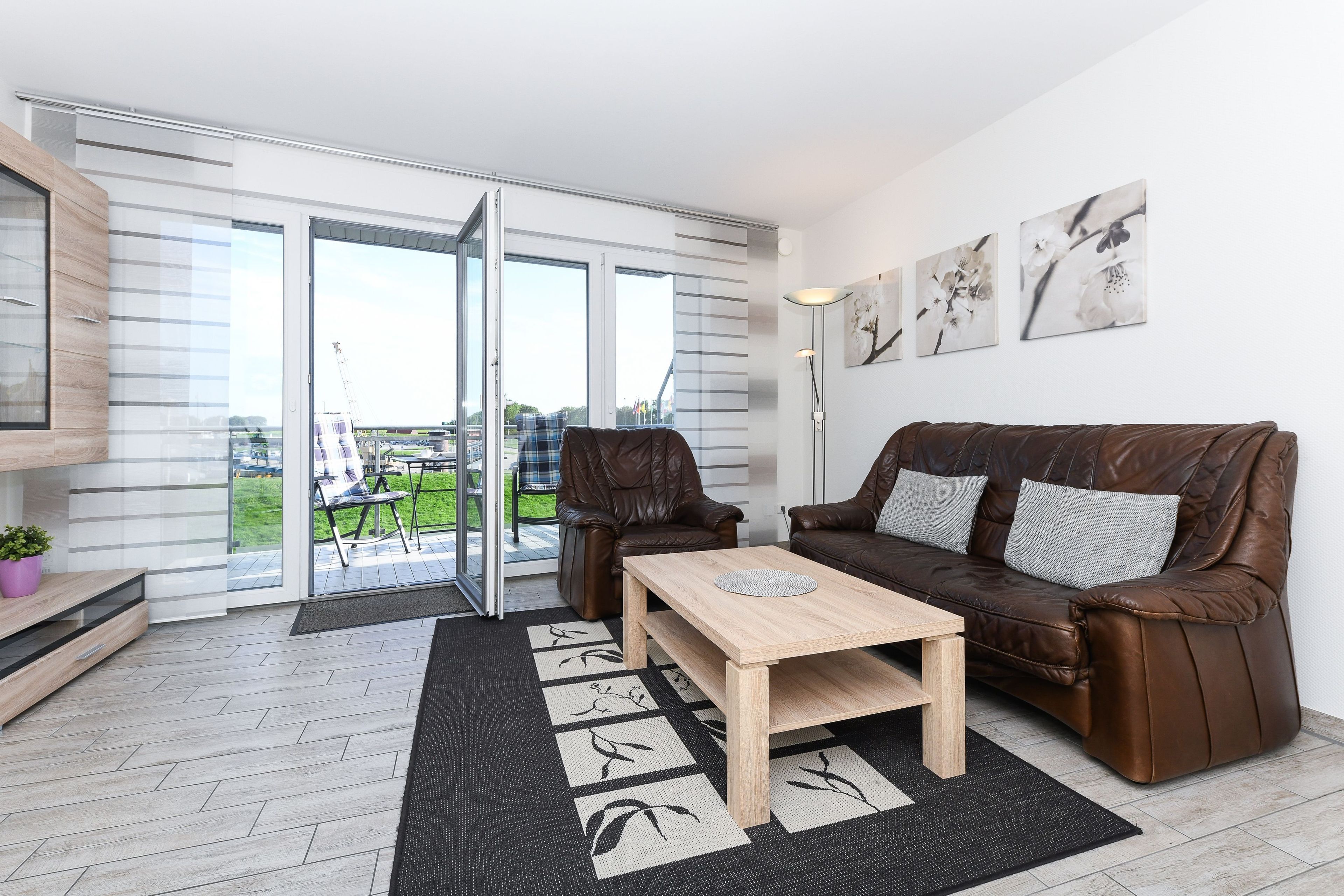 A modern living room with a brown leather sofa, a wooden coffee table, and a glass door leading to an outdoor area.