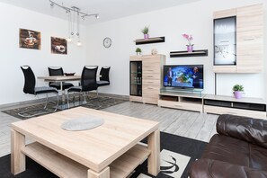 A modern living room with a wooden coffee table, black leather sofa, and a dining area with black chairs and a wooden table.