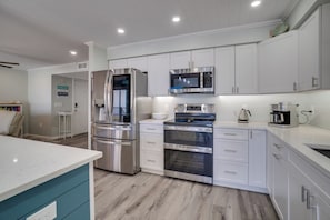 A modern kitchen with stainless steel appliances, white cabinetry, and a teal accent wall.
