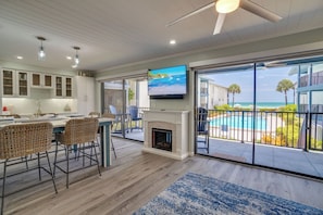 A modern kitchen with a dining area, a fireplace, and a large TV screen.