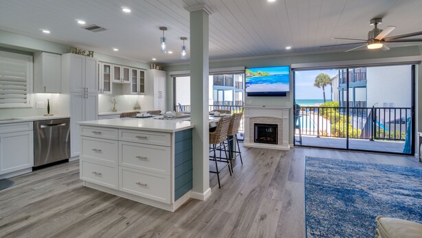 A modern kitchen with white cabinets, a central island, and a dining area with chairs.