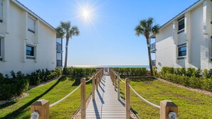 A wooden pathway leading to a beach with a clear sky and palm trees.