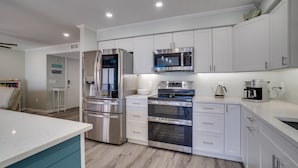 A modern kitchen with white cabinets, stainless steel appliances, and a teal accent wall.