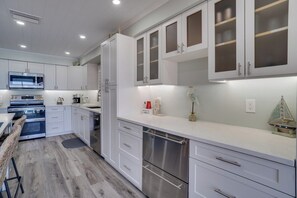 A modern kitchen with white cabinetry, stainless steel appliances, and a bar area with a wicker chair.