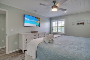 Une chambre à coucher comprenant un lit, un ventilateur de plafond, une télévision, une commode et une fenêtre.