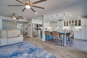 A modern kitchen with white cabinets, a dining area with wicker chairs, and a ceiling fan.