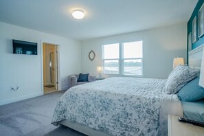Ein Schlafzimmer mit einem großen Bett, einem Fenster mit Ausblick, einer Tür und einem kleinen Tisch mit Lampe.