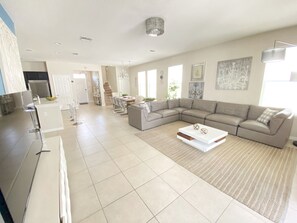 Un espacio habitable amplio con un sofá modular grande, una mesa de comedor y una zona de cocina.