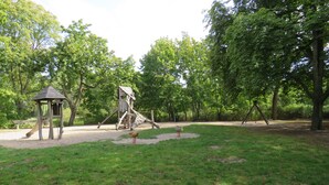 A park with a wooden play structure, a small pavilion, and a swing set.