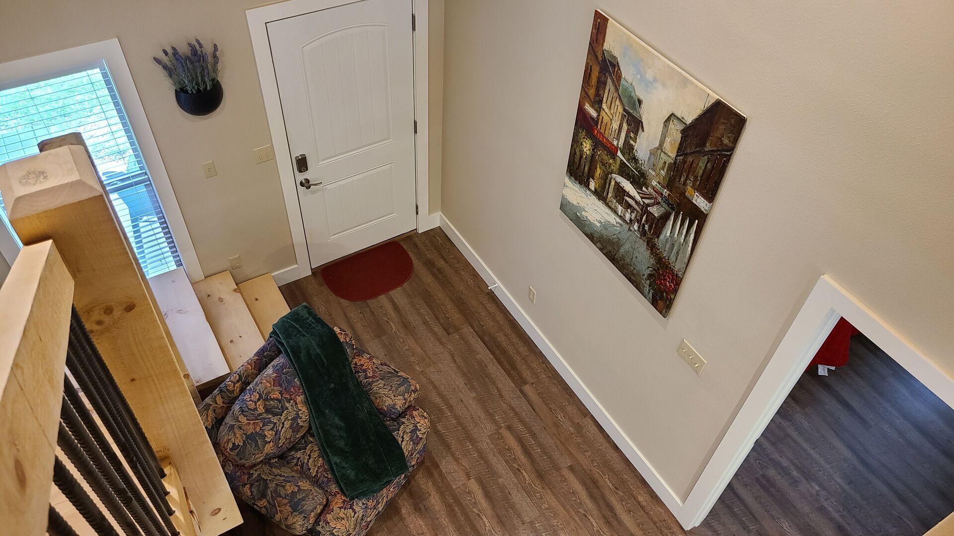 A hallway with a wooden staircase, a door, a red rug, and a painting on the wall.