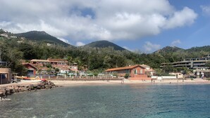 Kystområde med klart vand, en sandstrand og bygninger med røde tage.
