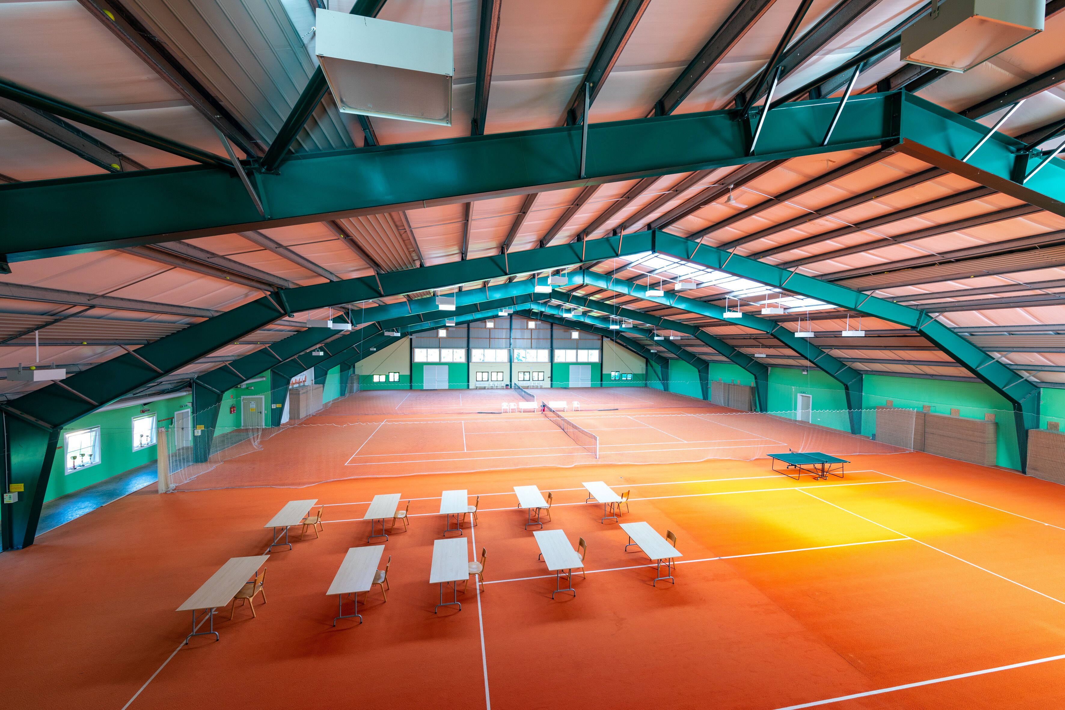 An indoor tennis court with tables and chairs arranged for spectators.