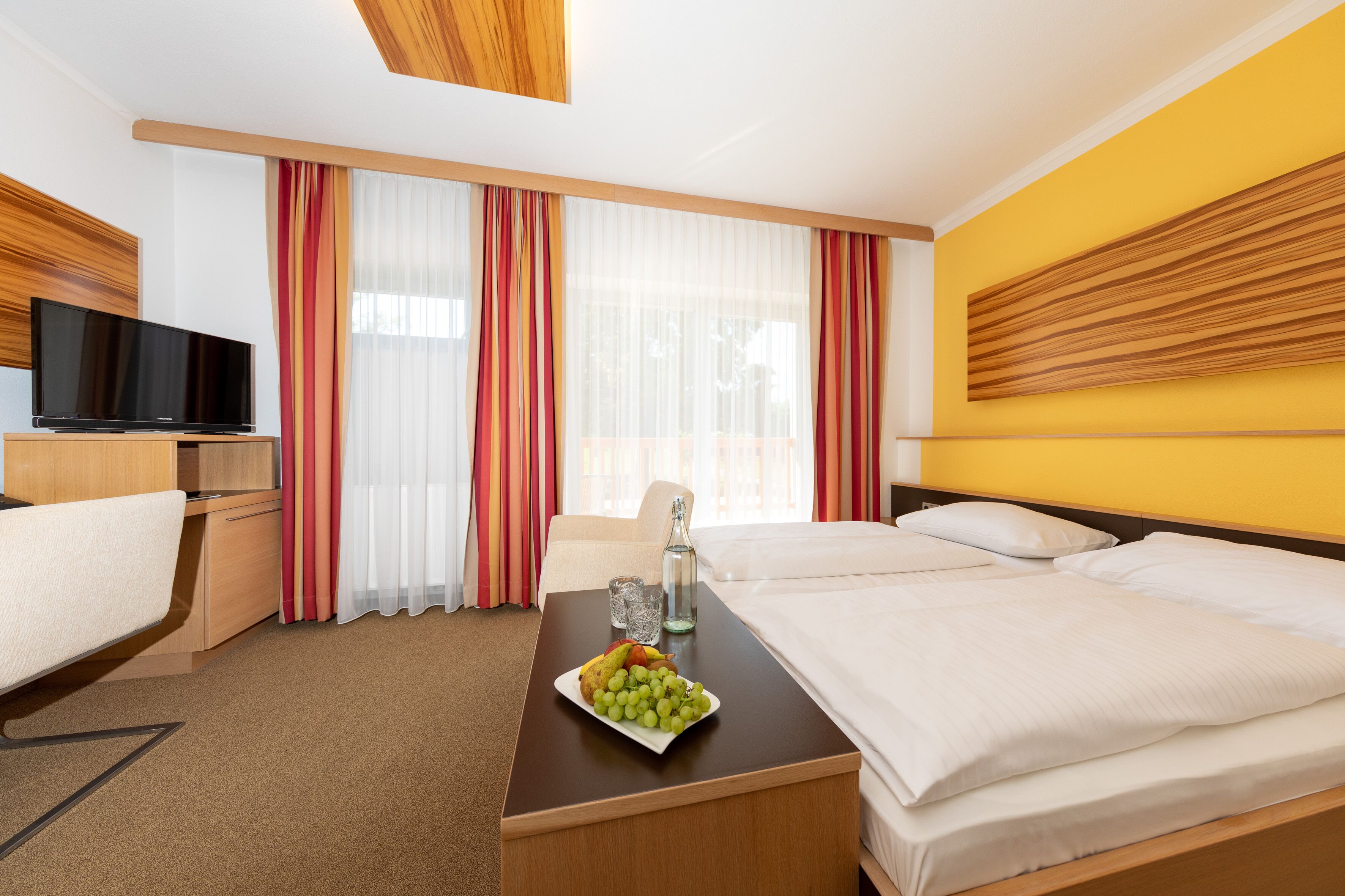 A hotel room with two beds, a desk with a television, a bottle, and a plate of fruit.