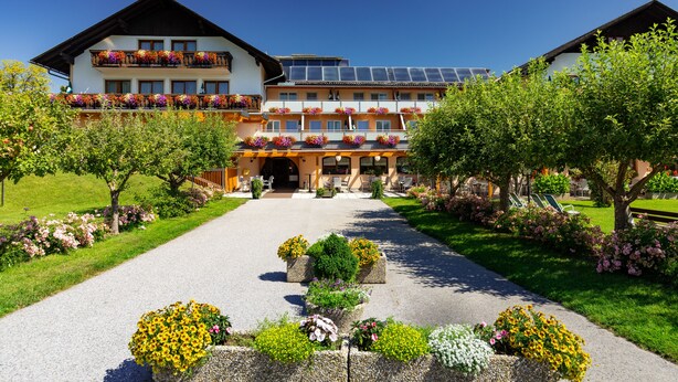 A hotel with a central entrance, multiple balconies with flower boxes, and a garden pathway.