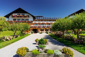 Un hotel con entrada central, varios balcones con jardineras y un camino de jardín.