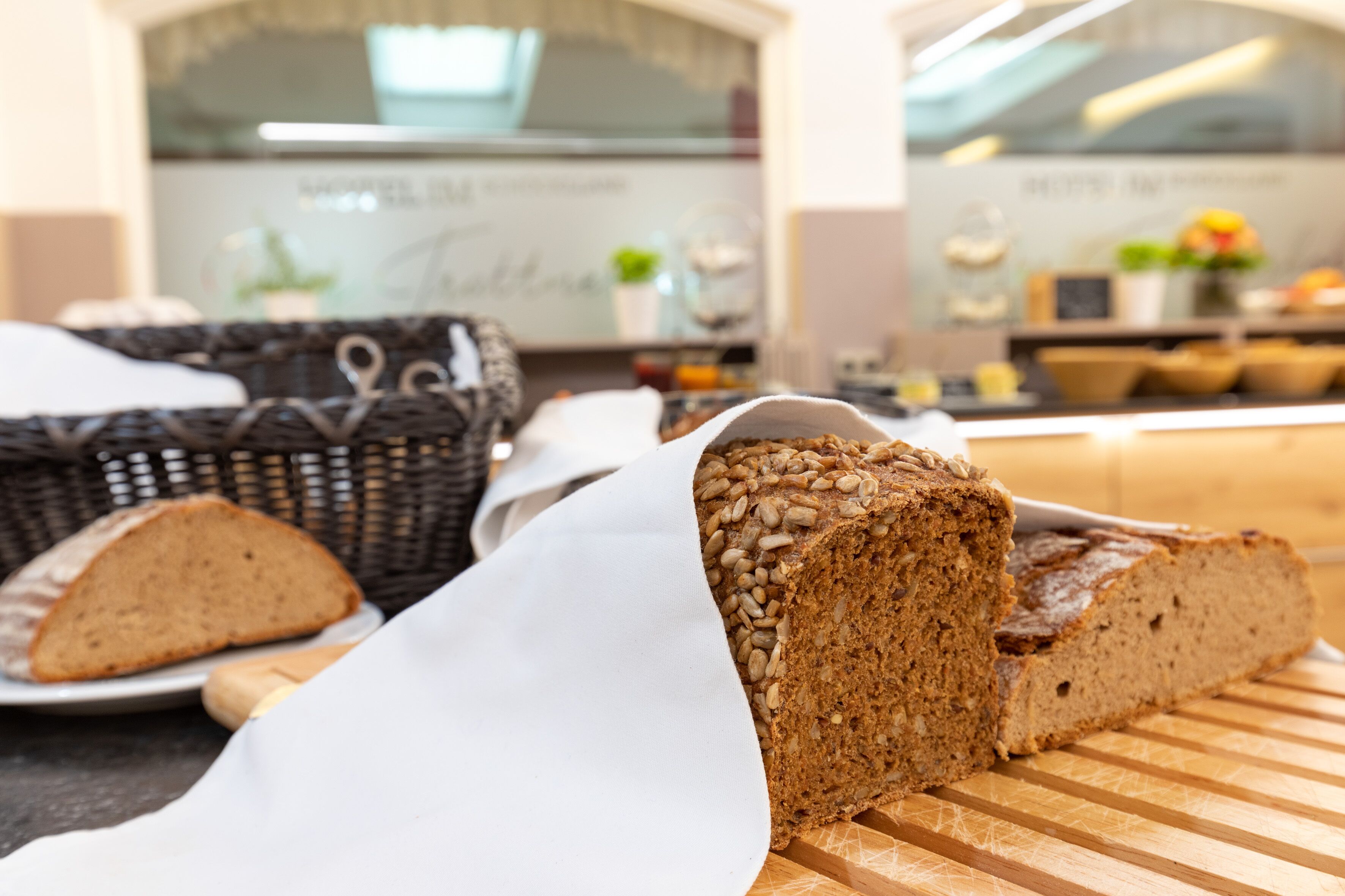 A loaf of whole grain bread on a cutting board with a wicker basket in the background.