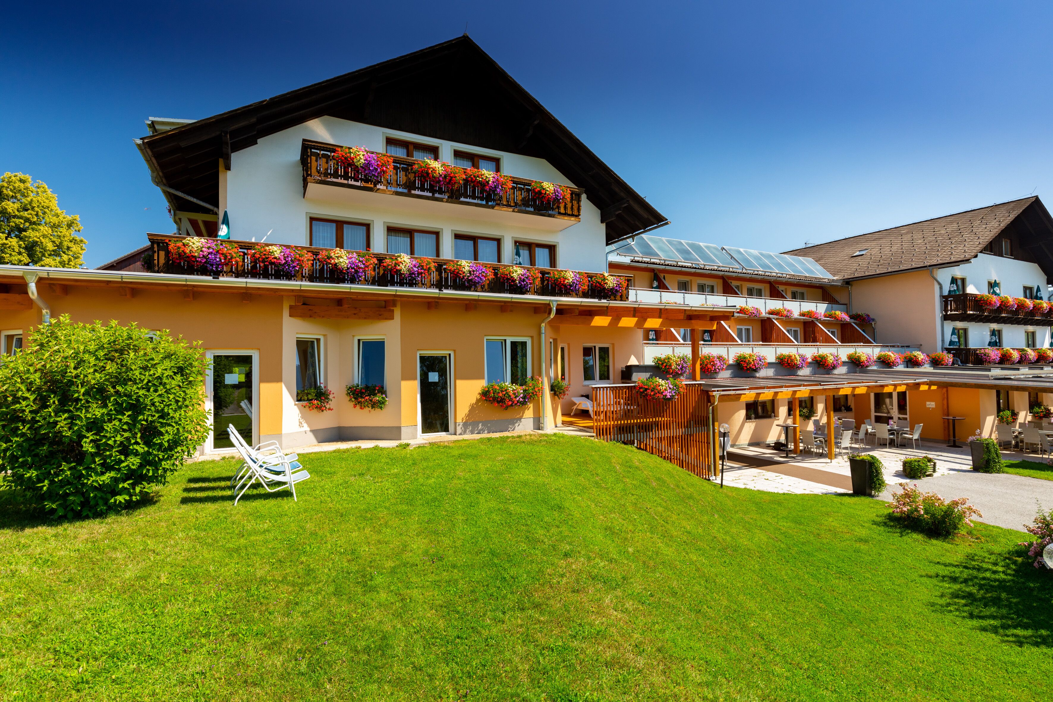 Ein Hotel mit mehreren Balkonen, die mit bunten Blumen geschmückt sind, einem gepflegten Rasen und einer überdachten Außenlounge.
