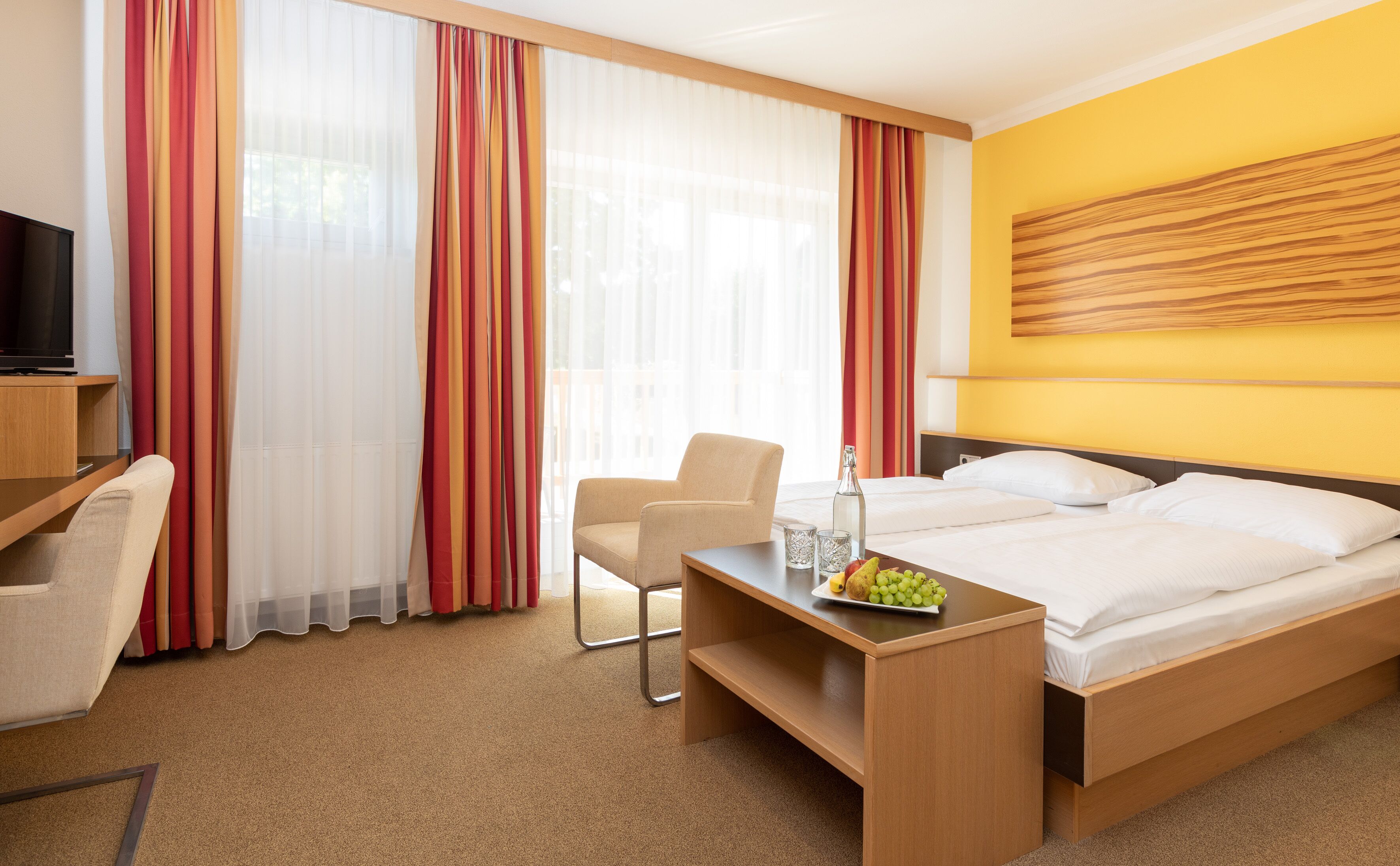 A hotel room with a bed, a desk with a chair, a TV, and curtains.