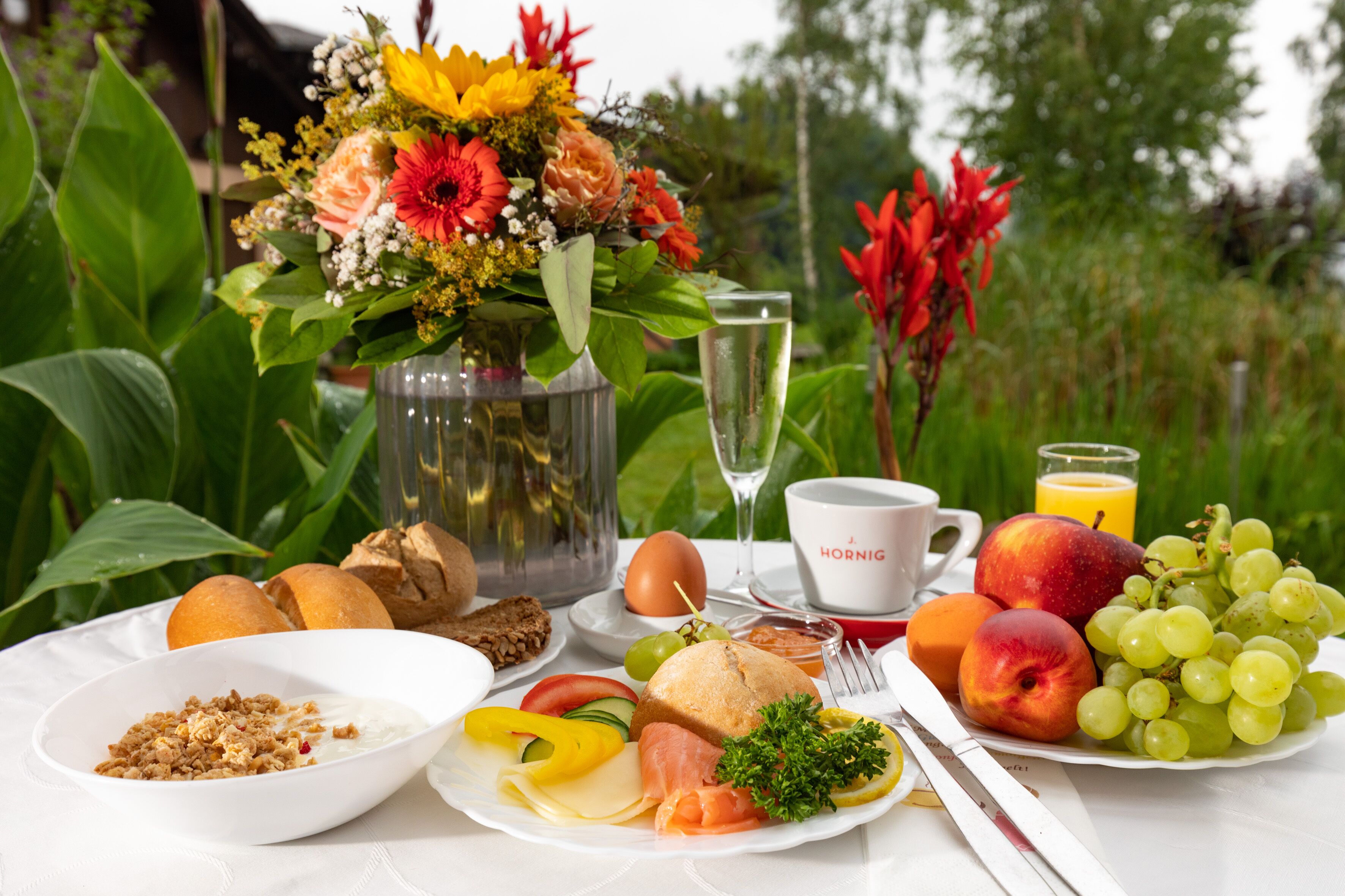 Una mesa de desayuno con una variedad de alimentos, como frutas, pan y un arreglo floral.