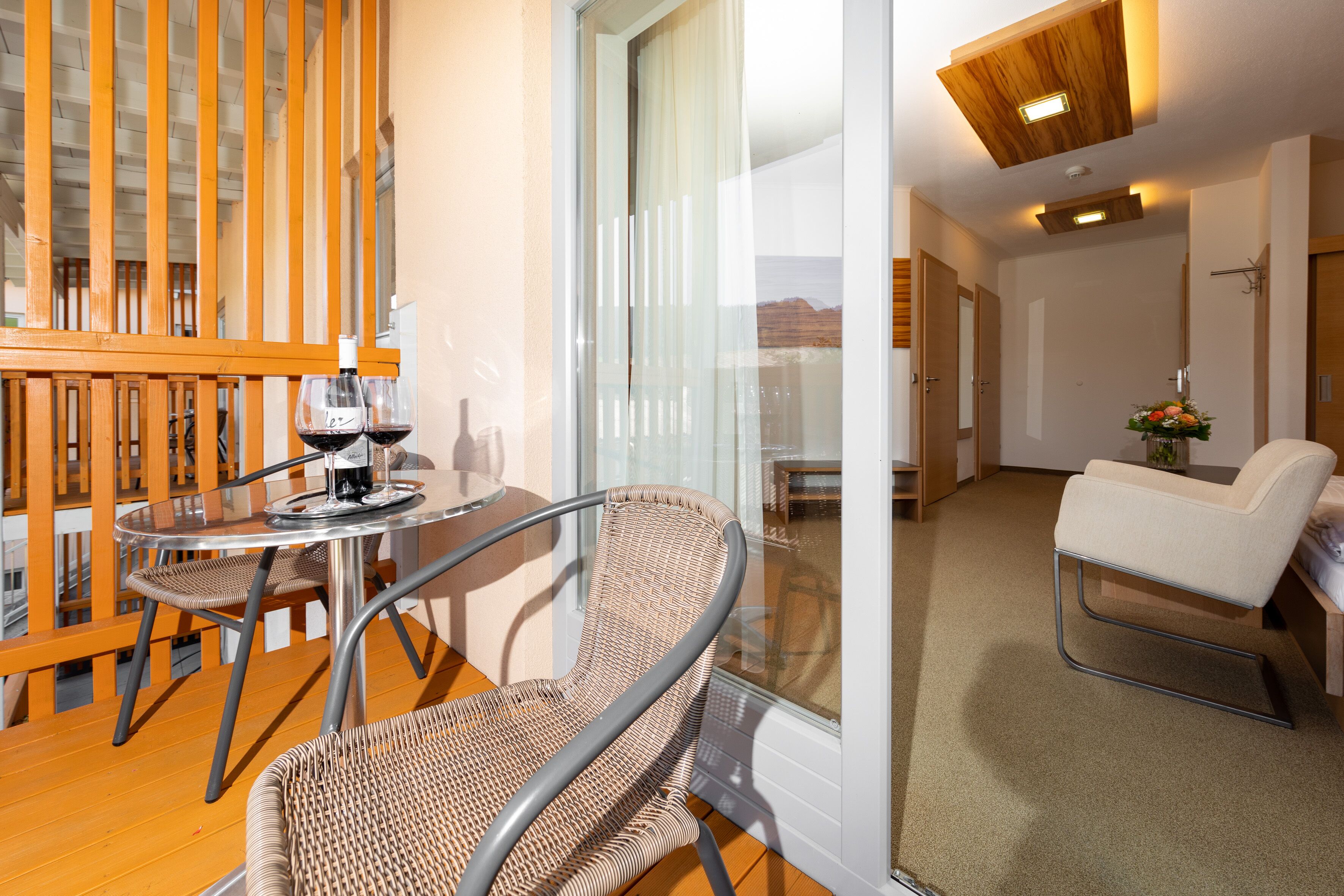 A balcony with wicker chairs, a table, and a bottle of wine.