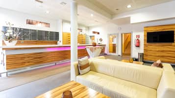 A modern hotel lobby with a reception desk, a sofa, a coffee table, and a television.