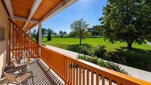 A balcony with a wooden railing, a table with chairs, and a view of a green lawn and trees.