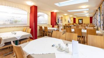 A dining area with multiple tables and chairs, a whiteboard with writing, and a red pillar.