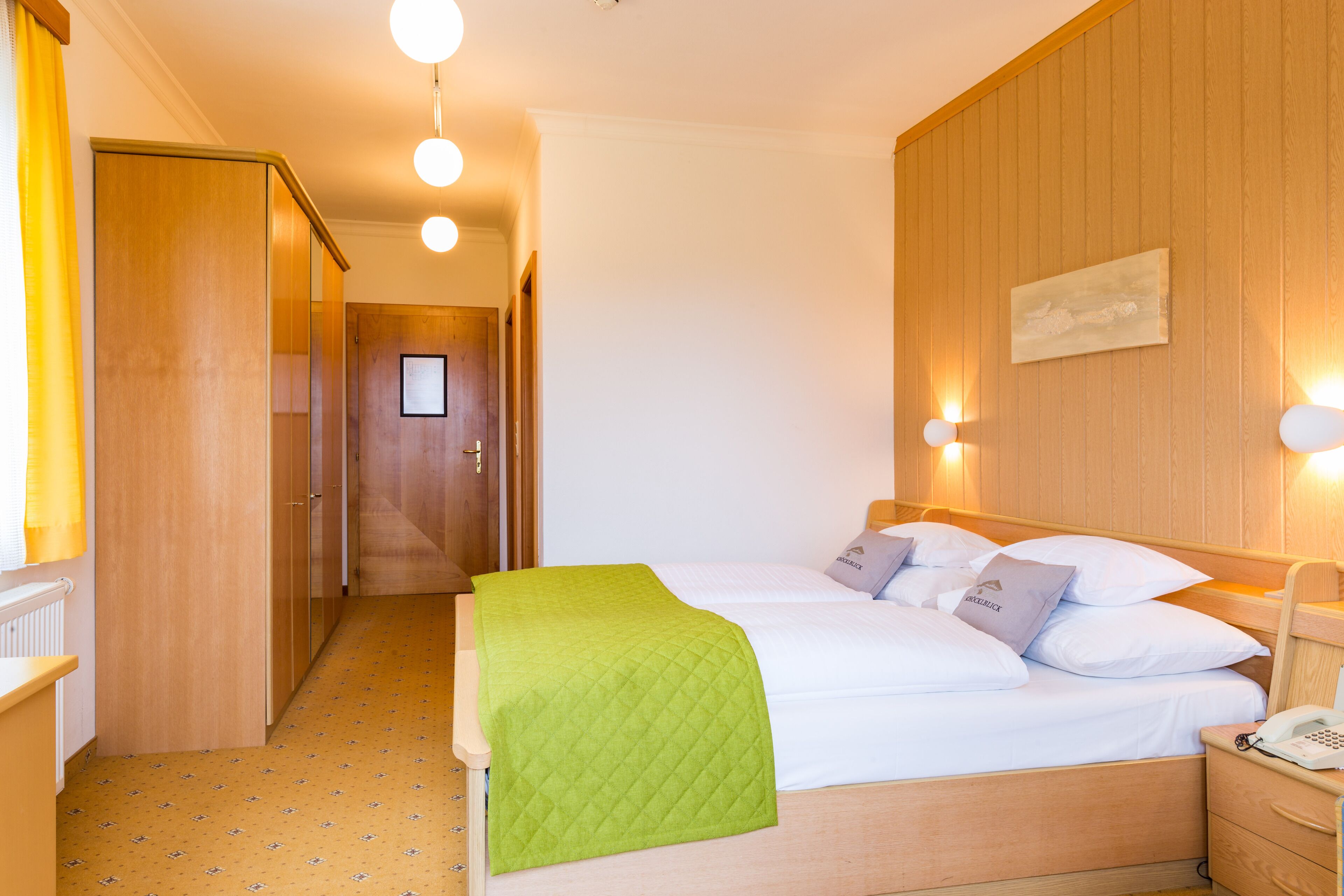 A hotel room with a bed, bedside table, and a wooden wardrobe.