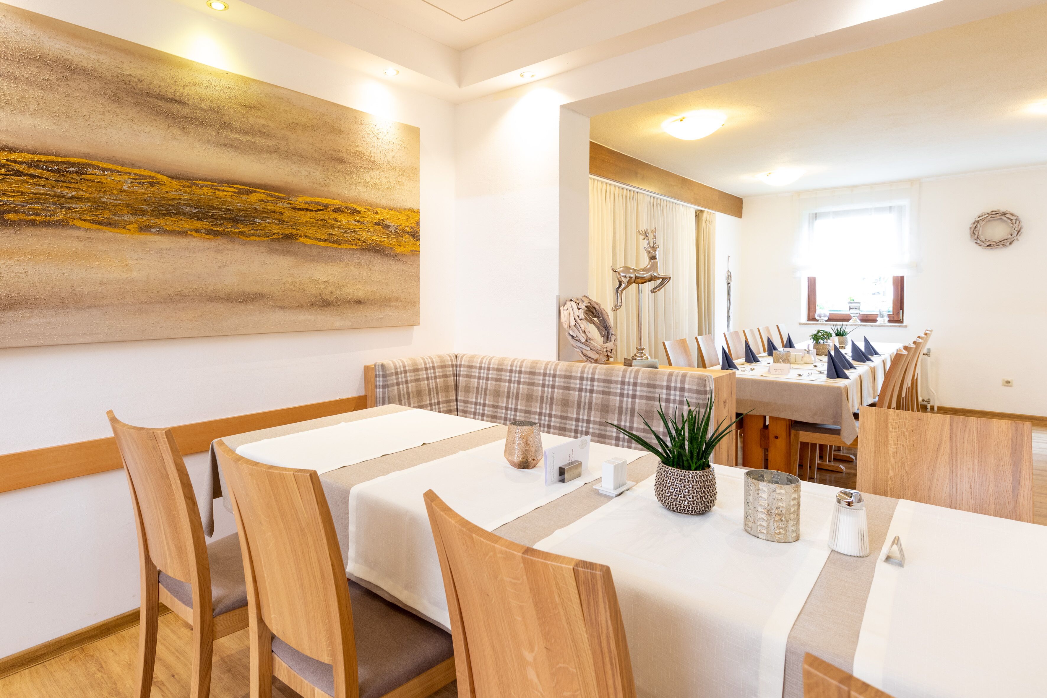 Un comedor con sillas y mesas de madera, un cuadro abstracto grande en la pared, y vista del salón comedor al fondo.
