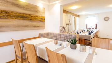 Un comedor con sillas y mesas de madera, un cuadro abstracto grande en la pared, y vista del salón comedor al fondo.